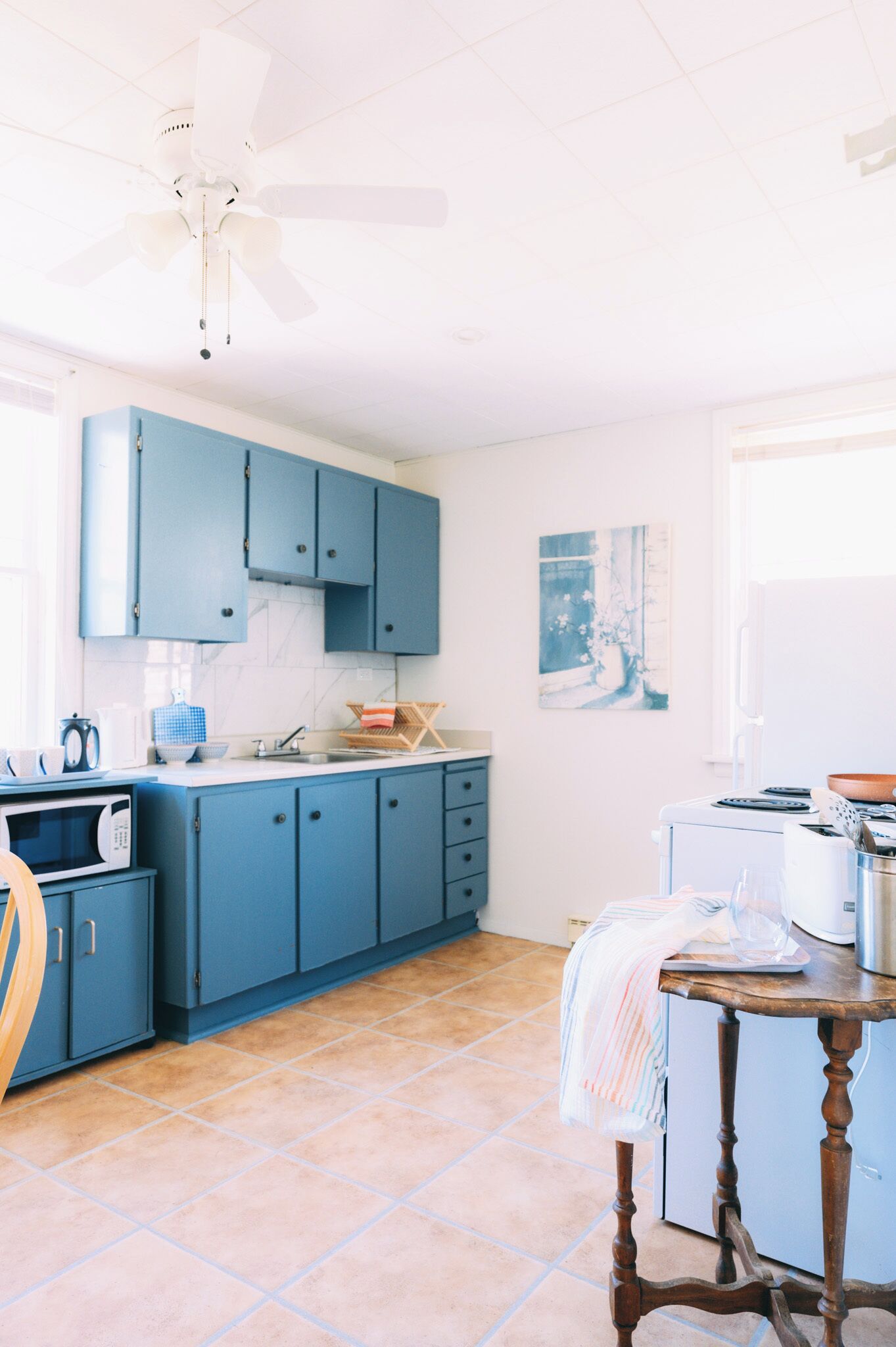 A kitchen with blue cabinets, a microwave, a sink, and a ceiling fan.