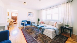 Un salon avec un canapé, un fauteuil bleu, une table basse et un tapis à motifs.