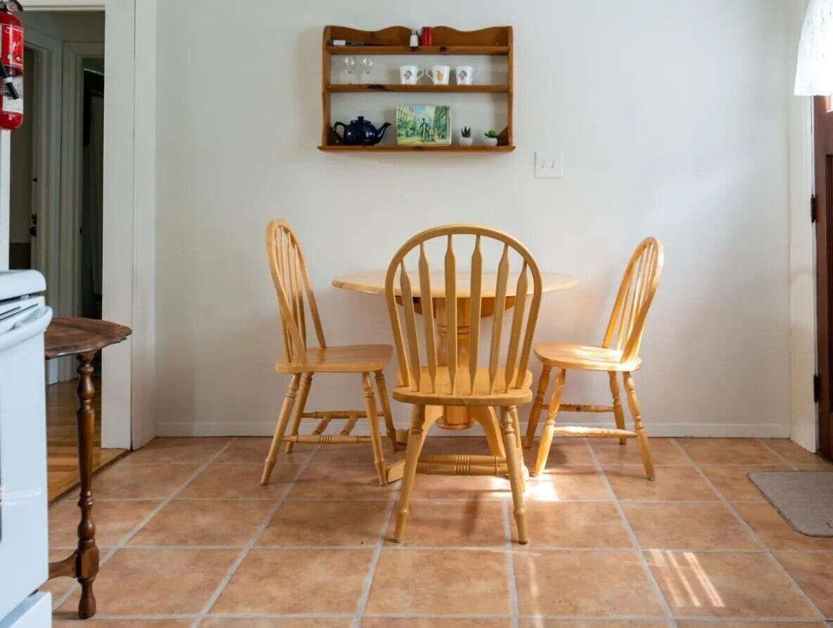 A dining area with a wooden table and four chairs, a shelf with kitchenware, and a fire extinguisher.
