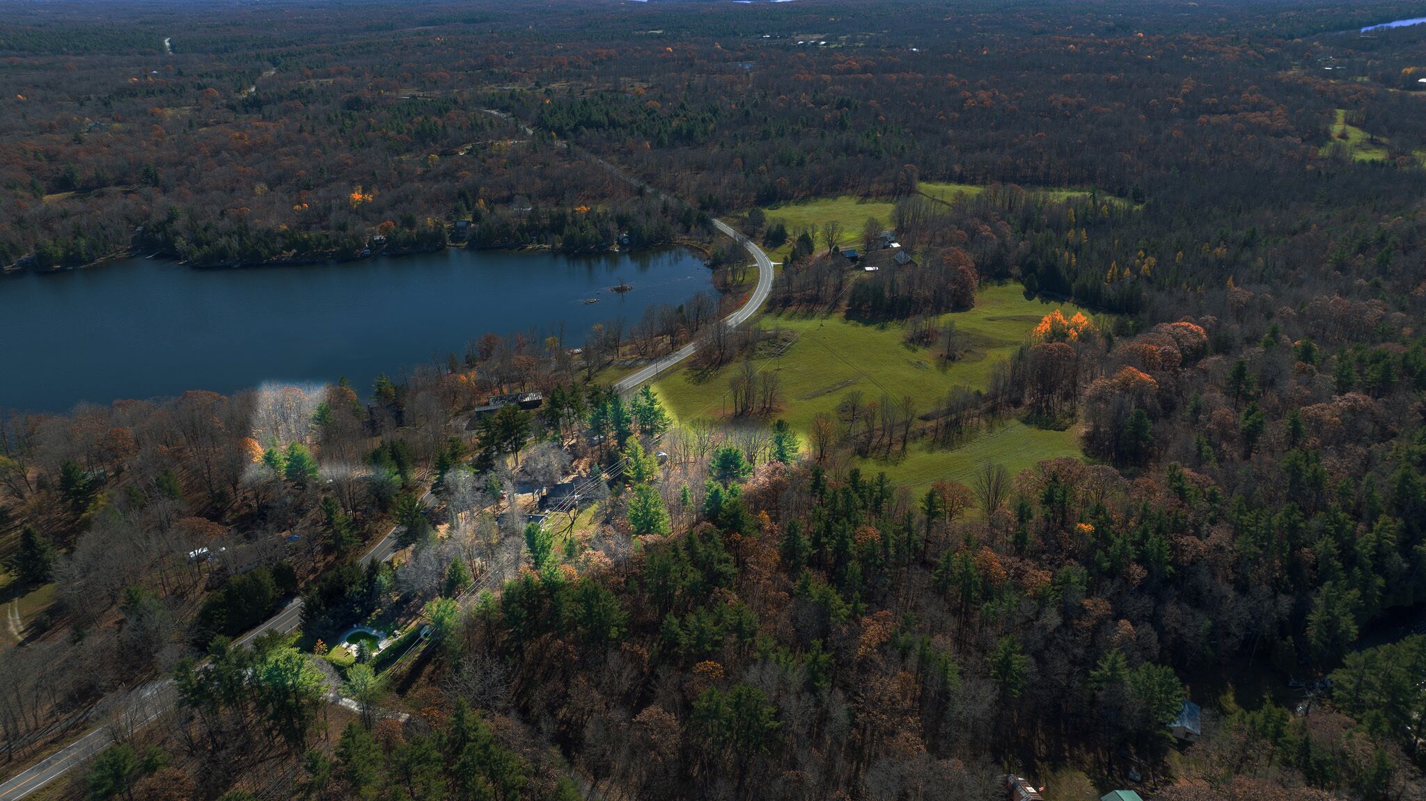 An aerial view of a lakeside property with a winding road, dense forest, and a small cluster of buildings.