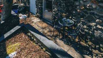 Une maison en pierre avec une cheminée, une porte et une petite terrasse avec une table et des chaises.