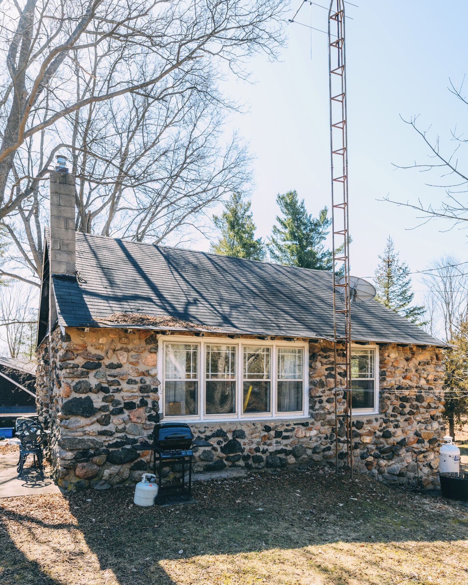 A stone house with a chimney, a satellite dish, and a ladder.