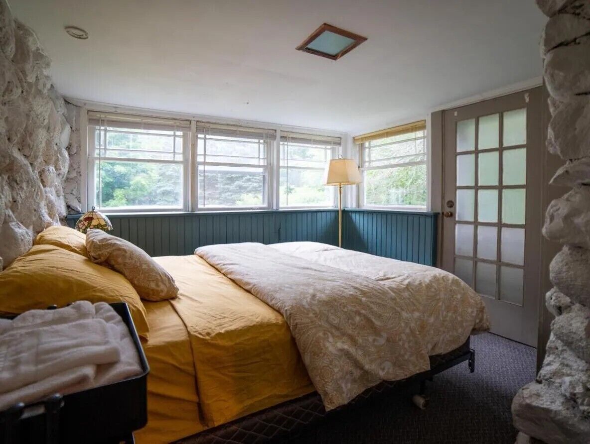 A bedroom with a bed, a lamp, a wardrobe, and a stone wall.