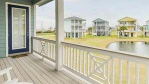Varanda coberta com vista para três casas de praia além da água.