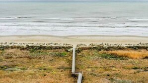 Paisagem costeira com céu claro, uma praia de areia e um caminho estreito em direção ao oceano.