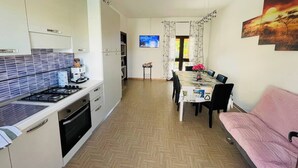 Une cuisine moderne équipée d’une cuisinière à gaz, d’un four et d’une machine à café. On y trouve également un coin repas avec une table et des chaises, ainsi qu’un canapé rose.
