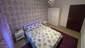 A bedroom with a bed, nightstand, wardrobe, and a chandelier. - Casa Gabriela: A Peaceful 2BR Gateway | Private Parking, AC, Near Beach (Viddalba)