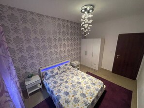 A bedroom with a bed, nightstand, wardrobe, and a chandelier. - Casa Gabriela: A Peaceful 2BR Gateway | Private Parking, AC, Near Beach (Viddalba)