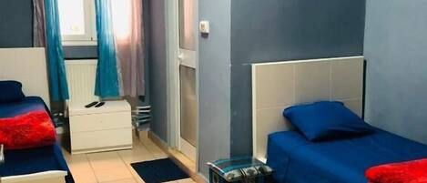Una habitación con dos camas, una ventana con cortinas, un radiador y una pequeña mesa.