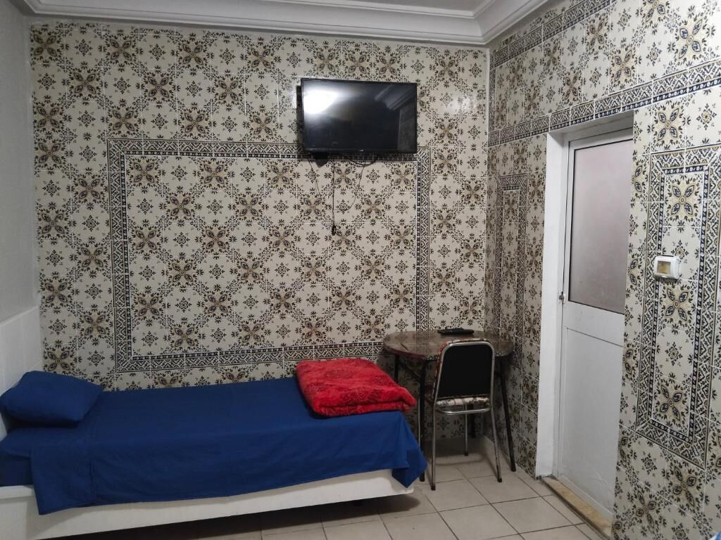 Una habitación con una cama, una mesita, una silla y un televisor montado en la pared.