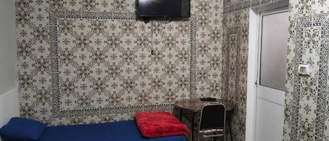 A room with a bed, a small table, a chair, and a TV mounted on the wall.