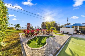 A landscaped area with a small pond, a play structure, and a seating area with umbrellas.
