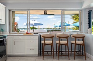 Eine moderne Küche mit einem großen Fenster und Blick auf das Wasser, inklusive einer Bar mit Hockern.
