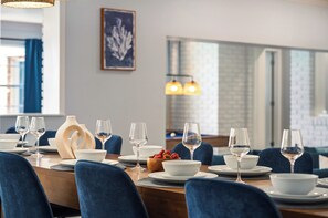 Ein Essbereich mit einem Holztisch, der für eine Mahlzeit gedeckt ist, blauen Polsterstühlen und einer Schale Erdbeeren.