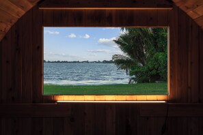 A wooden cabin with a window overlooking a body of water and a grassy area. - Waterfront Resort! Pickleball+Sauna+Pool+Hot Tub (West Palm Beach)
