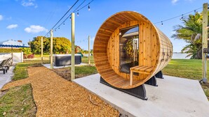 Een houten, cilindervormige constructie met een glazen deur, omgeven door een betonnen pad en buitenmeubilair.