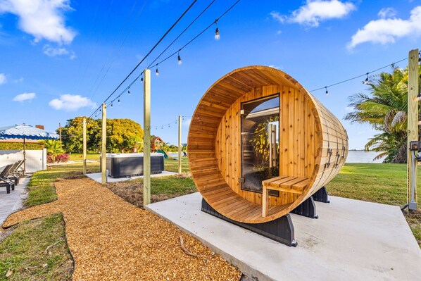 A wooden cylindrical structure with a glass door, surrounded by a concrete pathway and outdoor seating.