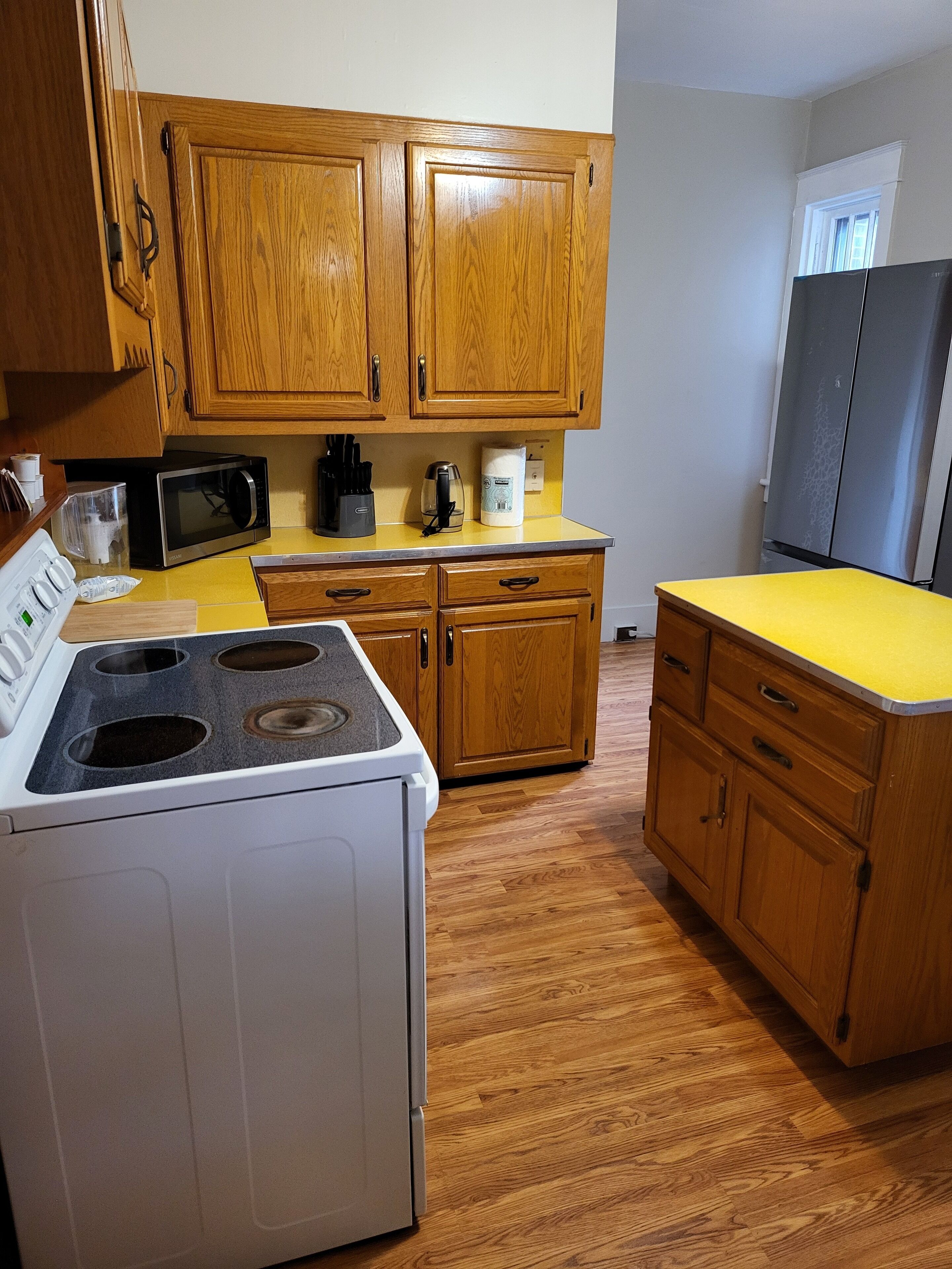 Una cocina con armarios de madera, microondas, estufa y refrigerador.