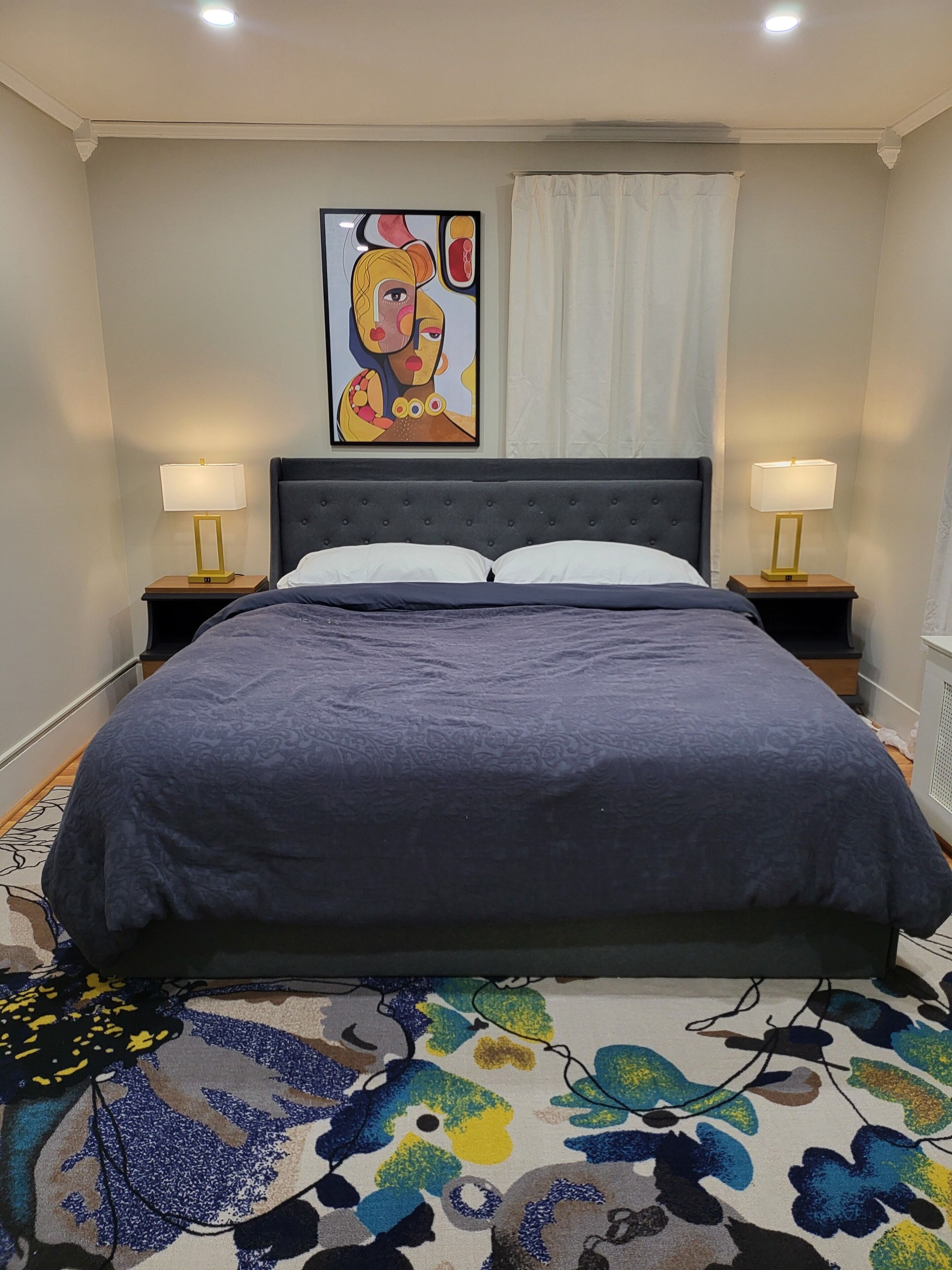 Ein Schlafzimmer mit einem großen Bett, zwei Nachttischlampen, einem Bild an der Wand und einem gemusterten Teppich.