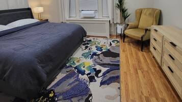 A bedroom with a bed, a chair, a dresser, a radiator, and a window with curtains.