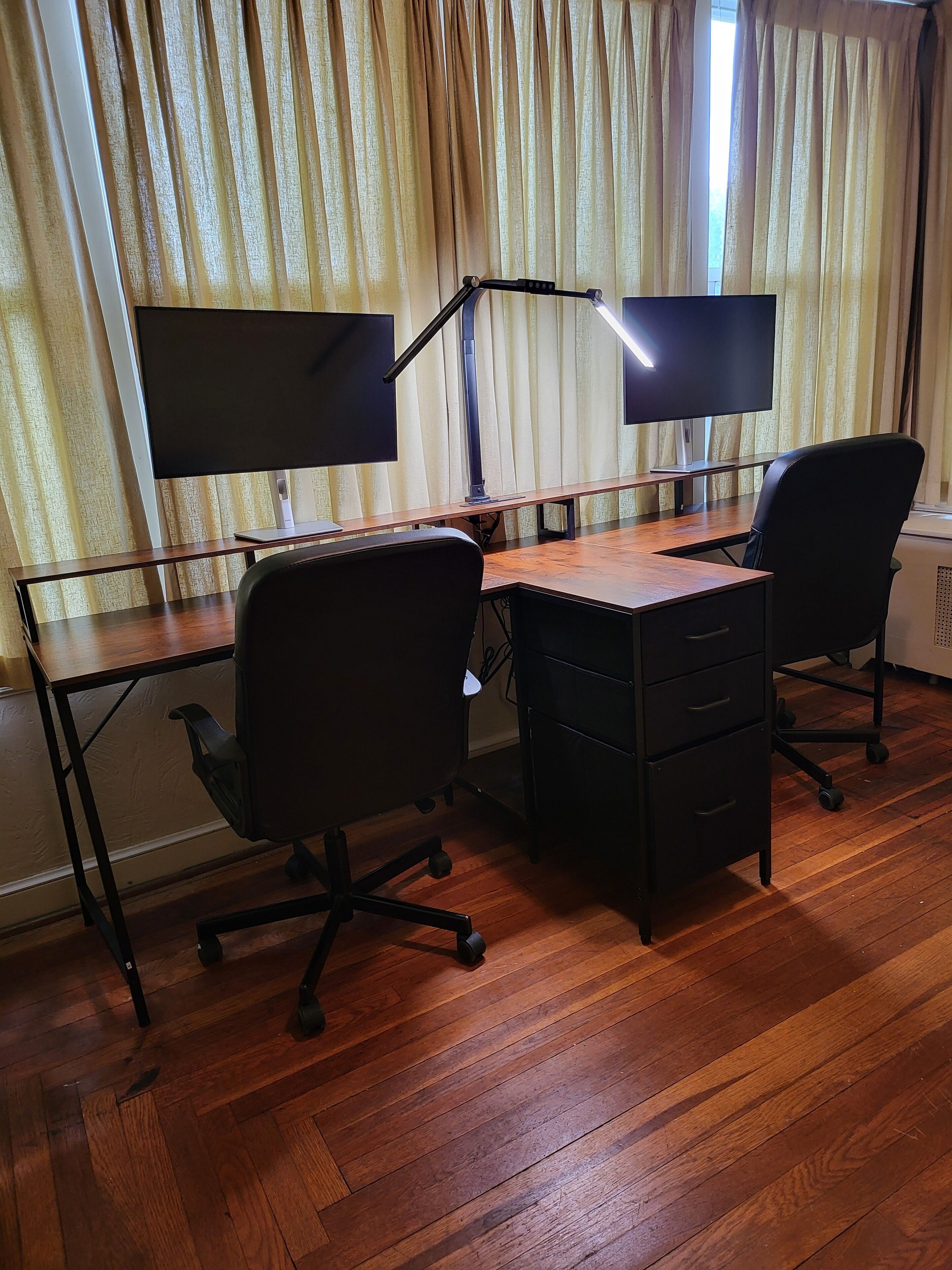 A room with two desks, each with a computer monitor and keyboard, and two office chairs.