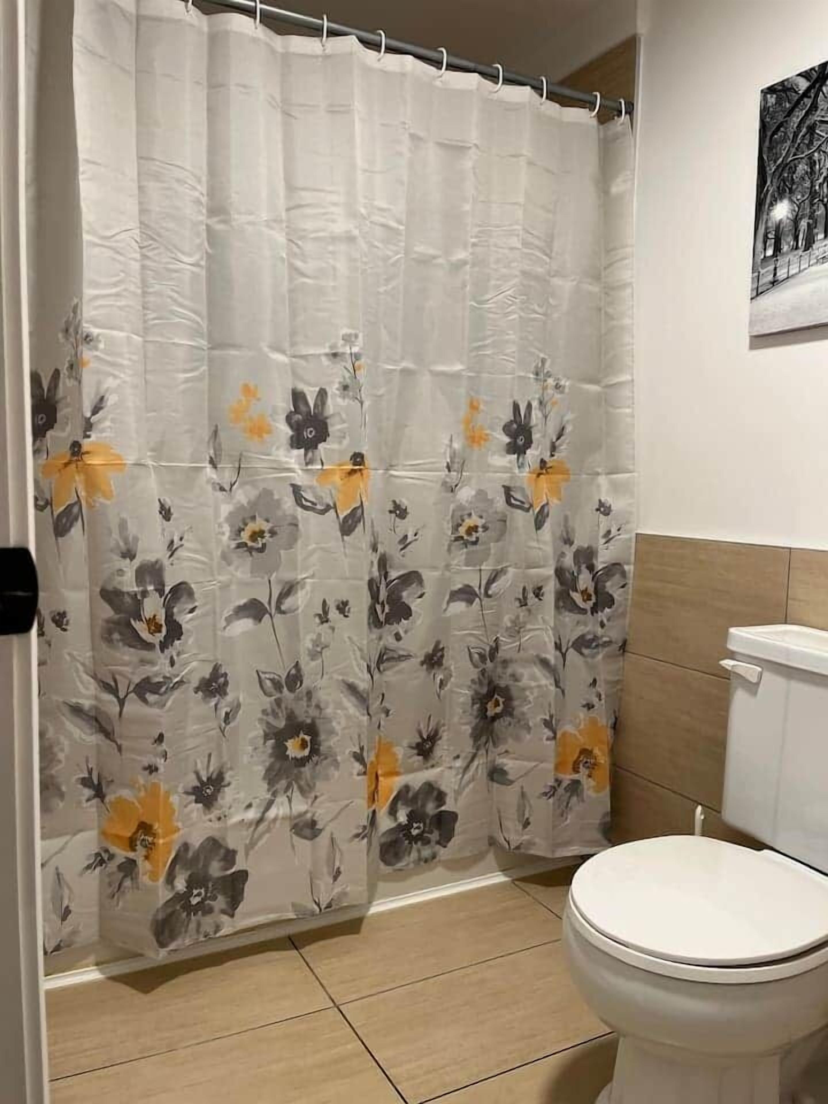 Een badkamer met douchegordijn met bloemmotieven, een toilet en een aan de muur hangend schilderij.