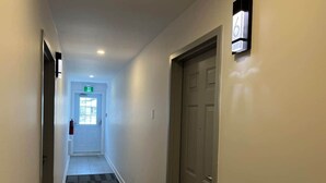Un couloir avec un sol recouvert de moquette, une porte sur la droite et une horloge au mur.