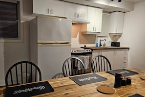 Una cocina compacta con gabinetes blancos, una estufa y un lavabo. Cuatro sillas rodean una mesa de madera con individuales negros.