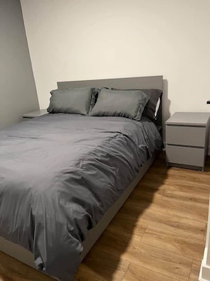 Un dormitorio con cama, mesitas de noche y suelo de madera.