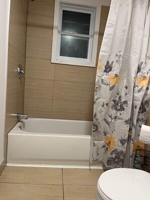 A bathroom with a bathtub, a window, and a toilet.