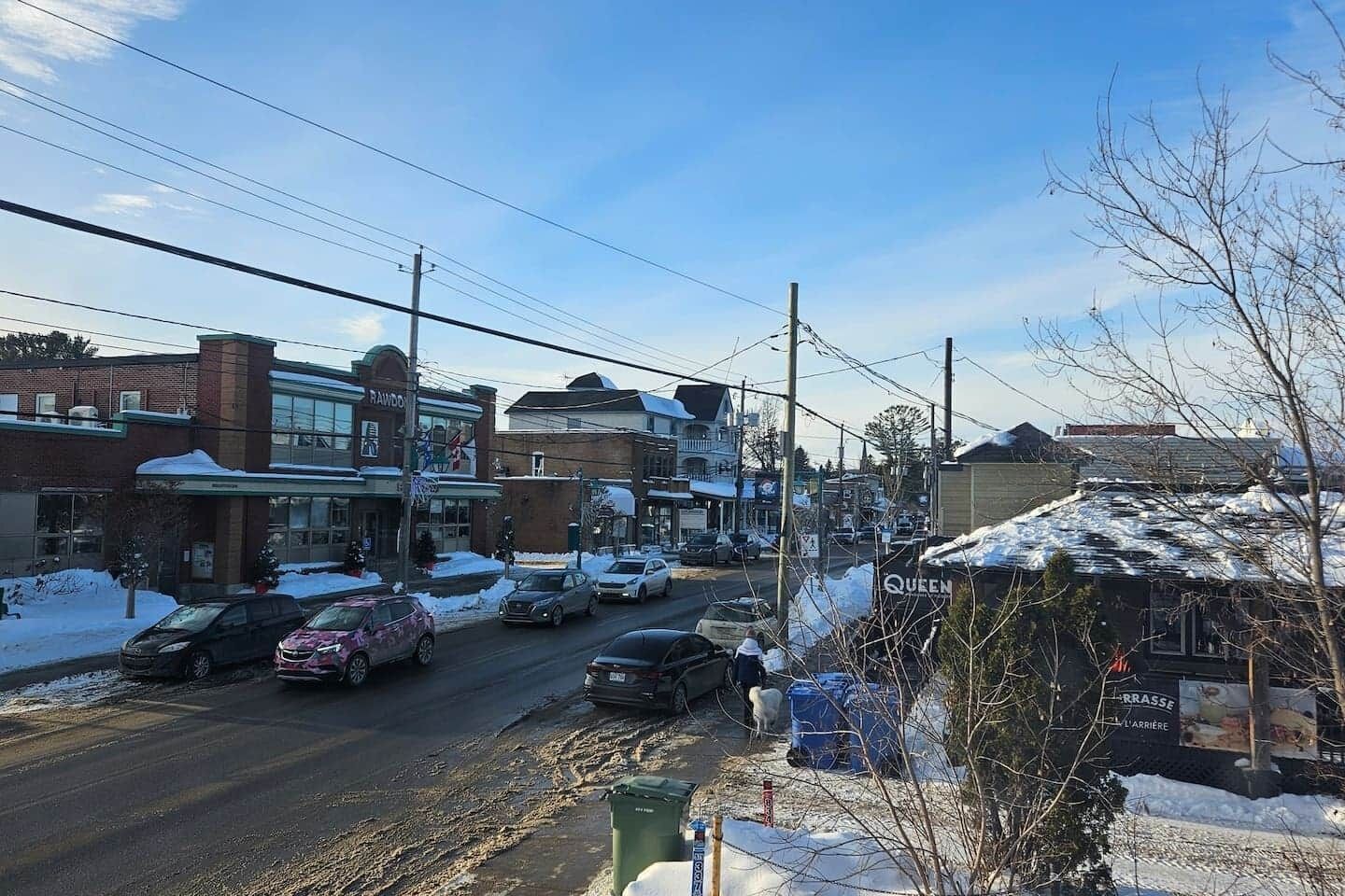 A street view with buildings, cars, and a sign for 'Queen.'