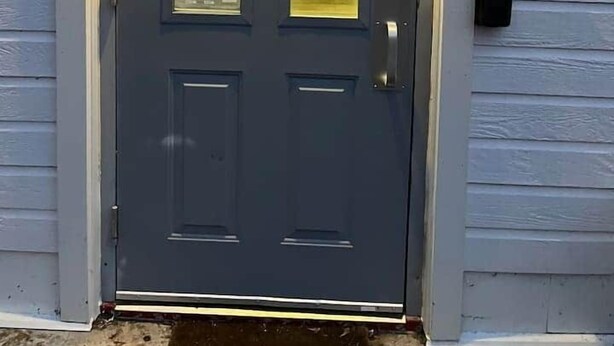 Une porte d’entrée grise avec un panneau en verre, une boîte aux lettres et un système de verrouillage à clavier.