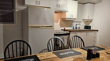 Una cucina compatta con mobili bianchi, un fornello e un lavandino. Quattro sedie circondano un tavolo di legno con sottopiatti neri.