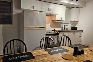 Een compacte keuken met witte kastjes, een fornuis en een spoelbak. Er staan vier stoelen rond een houten tafel met zwarte tafelmatten.