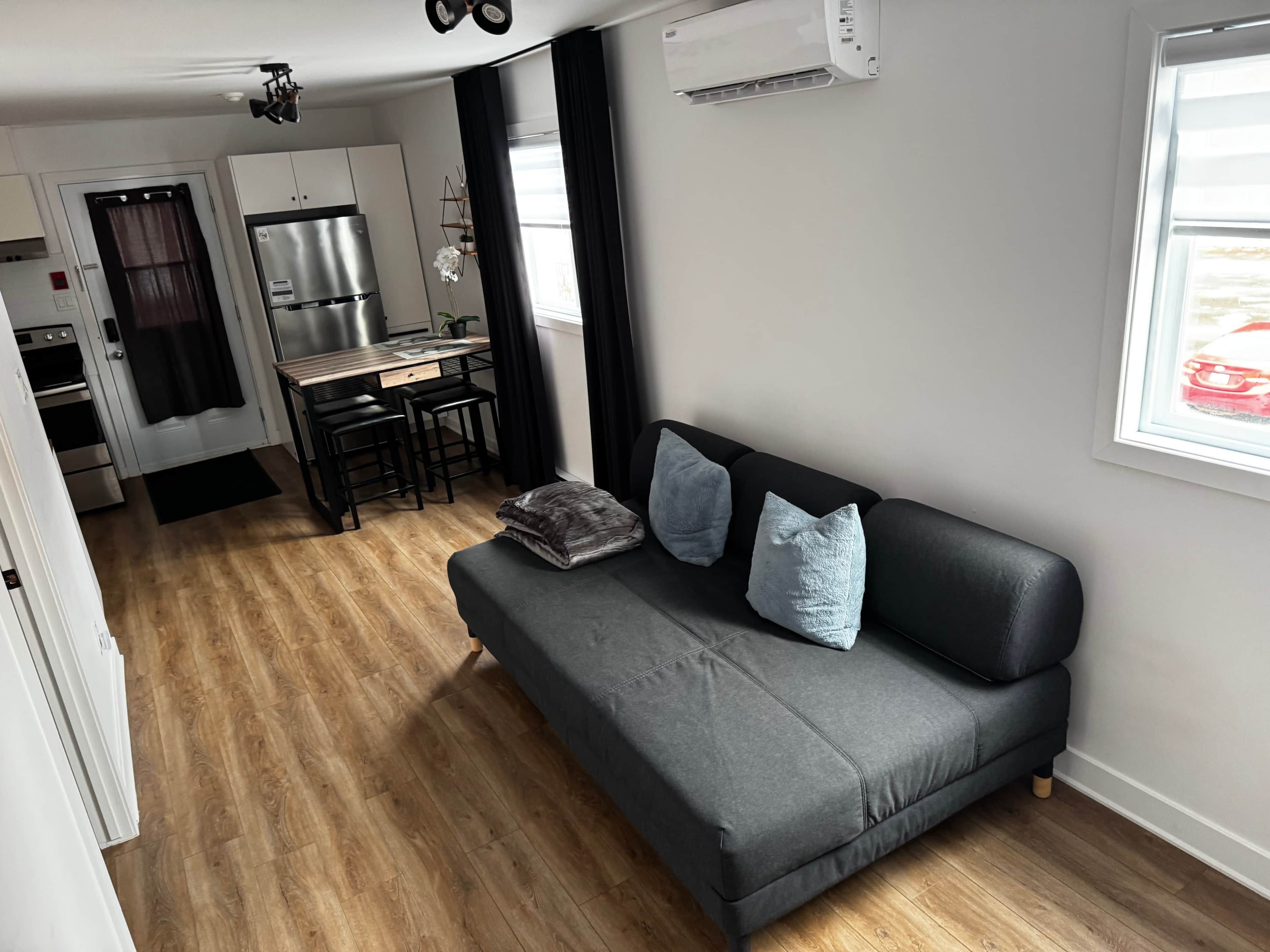A compact living space with a kitchenette, a sofa with cushions, and a window with a view.