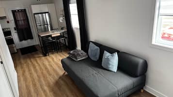 A compact living space with a kitchenette, a sofa with cushions, and a window with a view.