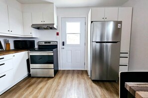 A compact kitchen with white cabinets, a stainless steel refrigerator, a built-in oven, and a microwave.