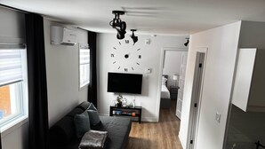 A modern apartment with a living area featuring a sofa, a TV, and a wooden dining table.