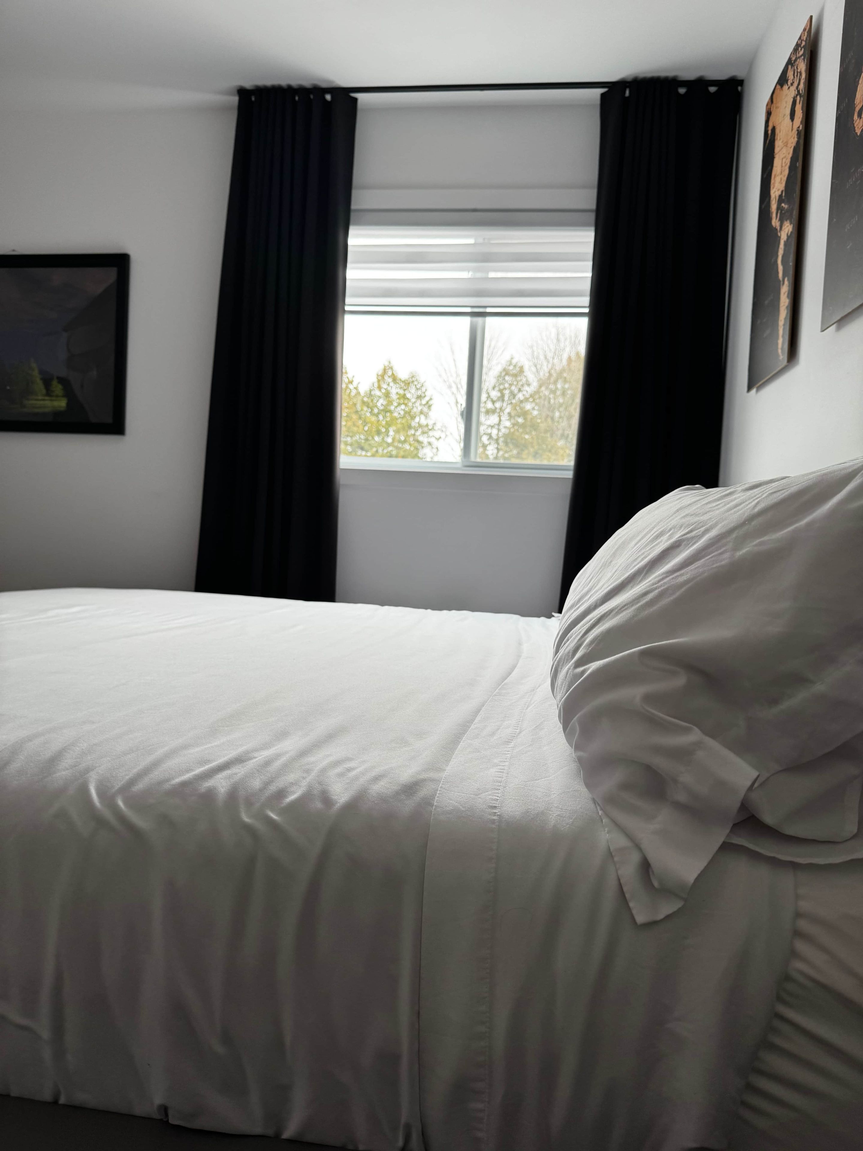 A room with a bed, a window with curtains, and a painting on the wall.