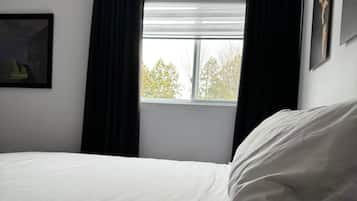 A room with a bed, a window with curtains, and a painting on the wall.