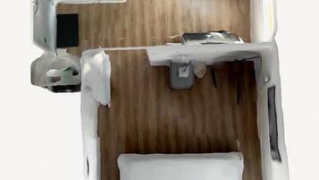 Vista cenital de una habitación de hotel con cama, escritorio, silla, mesita y armario.