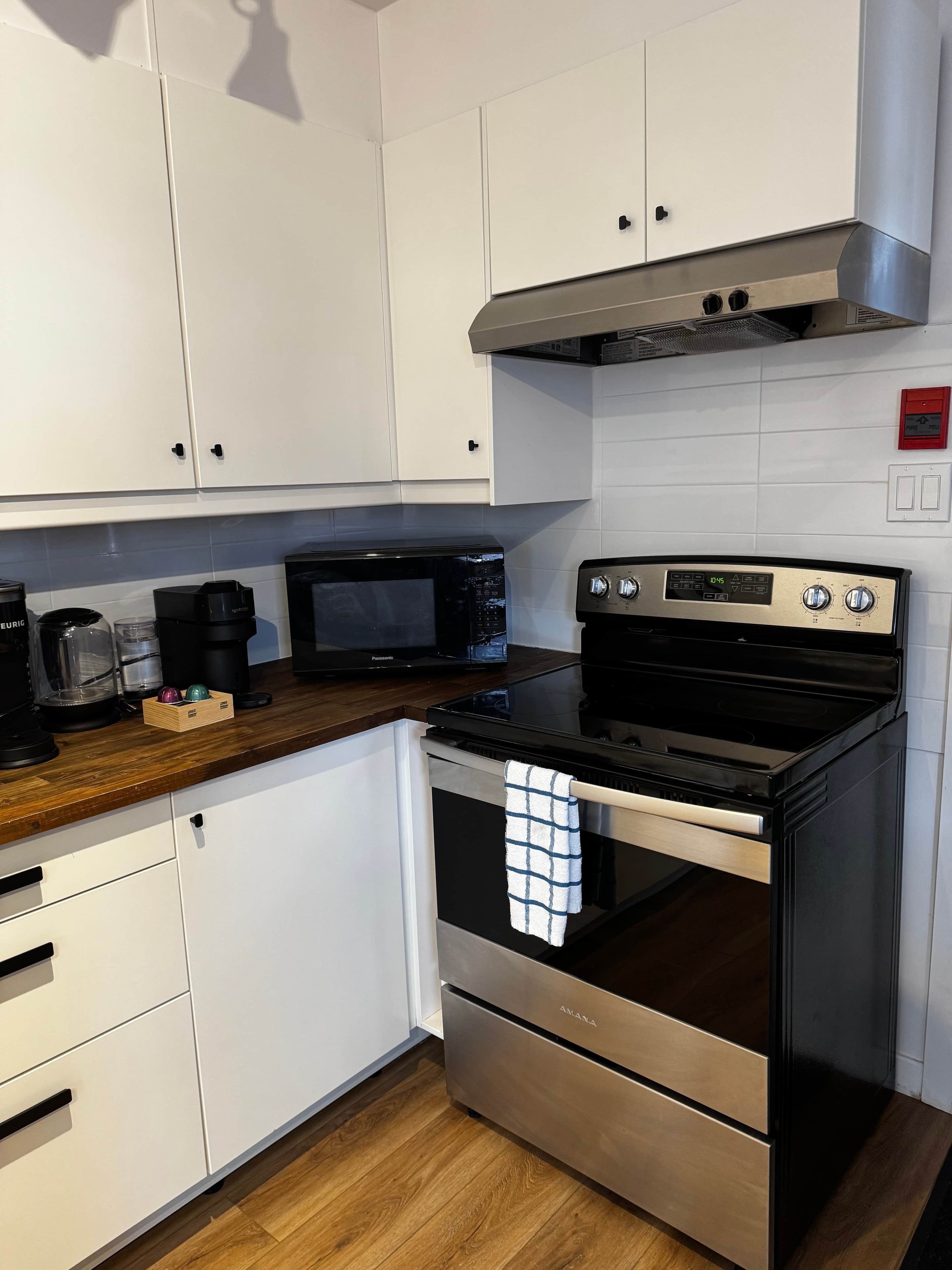 Een keuken met witte kastjes, een zwarte magnetron, een roestvrijstalen fornuis en een houten aanrecht.