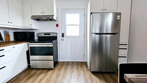 A compact kitchen with white cabinets, a stainless steel refrigerator, a built-in oven, and a microwave.