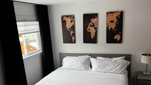 A modern bedroom with a large bed, a window with blinds, and three world map artworks on the wall.