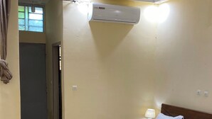 A hotel room with a bed, a chair, a desk, and an air conditioning unit. - Cocody Riviera 3, Splendid studio #04 quiet and peaceful residential area (Abidjan)