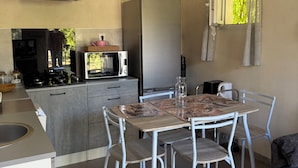 A compact kitchen with a dining area, featuring a refrigerator, stove, microwave, and a table with chairs. - Cosy and bright gîte with private pool for rent (Bollène)