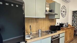 A modern kitchen with light blue cabinets, a black refrigerator, a wooden countertop, and a clock on the wall. - St.Peter YH (Roma)