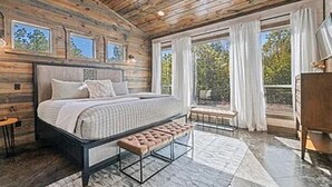 Ein Schlafzimmer mit Holzboden, einem großen Bett mit Sitzbank, einem Fenster und Blick ins Freie.