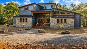 Ein modernes, zweistöckiges Haus mit Natursteinfassade, großen Fenstern und einer Holzterrasse.