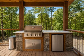 An outdoor kitchen with a grill, a refrigerator, and a stone wall. - Whippoorwill Creek -Stunning Cabin on a Creek w/ Games, Hot Tub, & More... (Broken Bow)